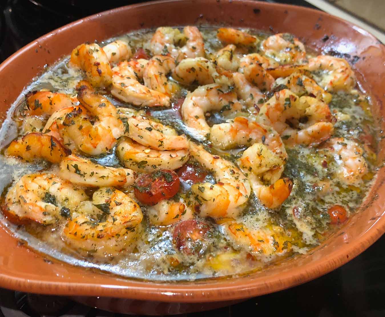 Spicy baked shrimp in garlic olive oil sauce with tomatoes, herbs, and spaghetti.